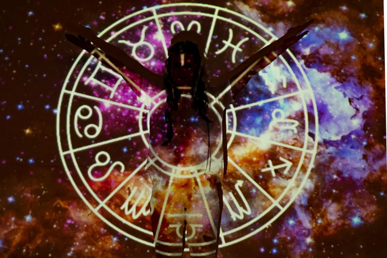 Silhouette of person extending arms against zodiac symbols and cosmic background, esoteric