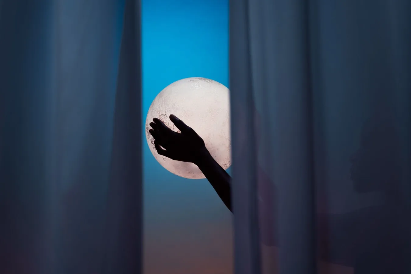 Silhouette hands framed between curtains, reaching for a bright full moon in the night sky