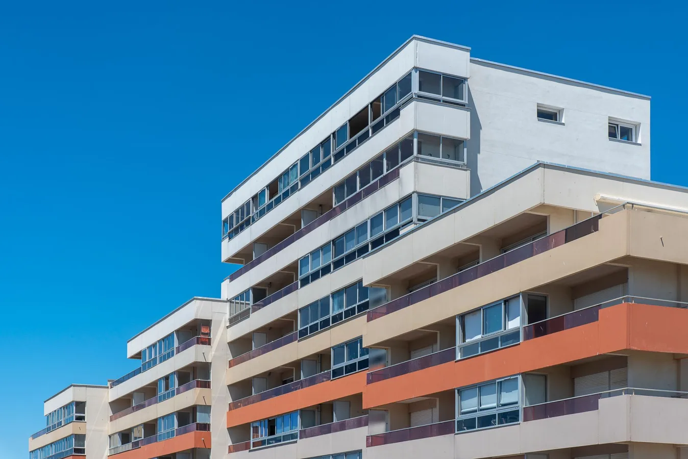 Contemporary multi-story apartment buildings with balconies under a clear blue sky, showca