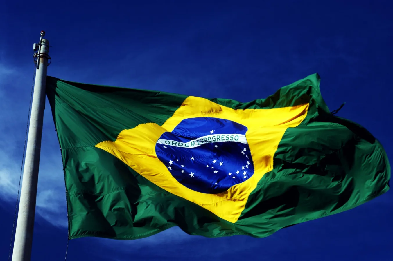 A dynamic shot of the Brazilian flag waving on a flagpole with a clear blue sky background