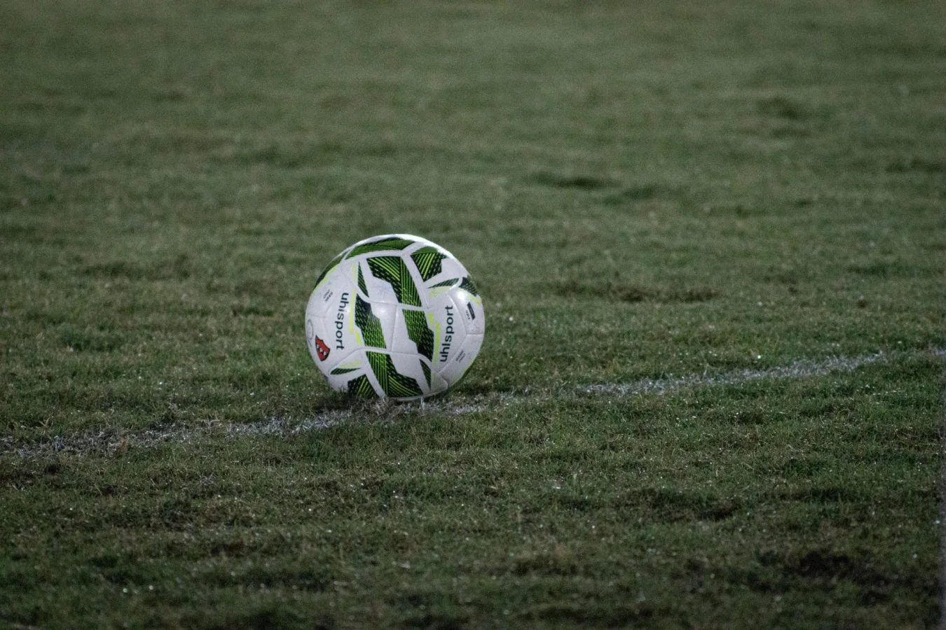 A soccer ball resting on a grass field, captured during nightfall with visible dew.