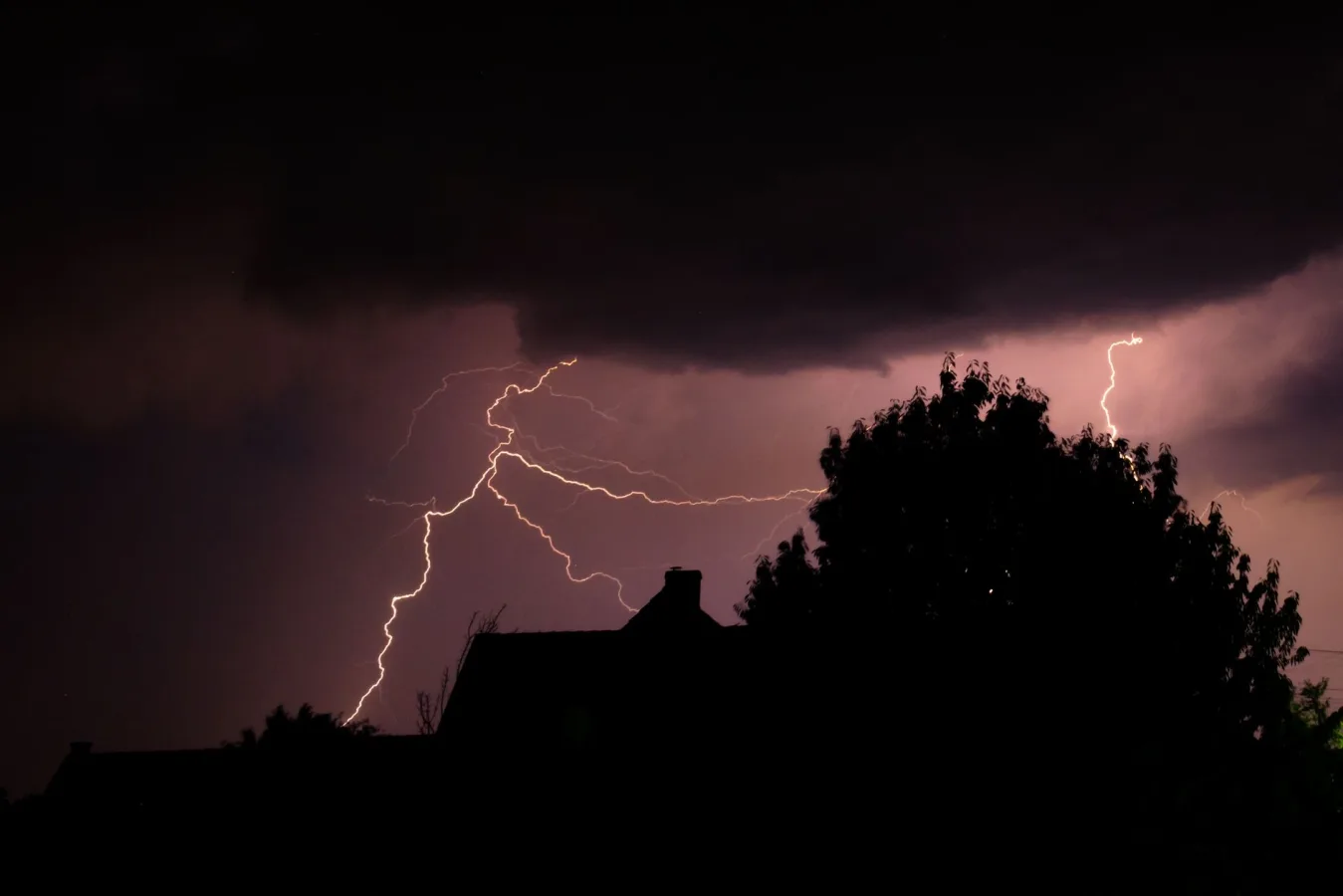 A striking lightning bolt illuminates the dark sky over silhouetted houses during a powerf
