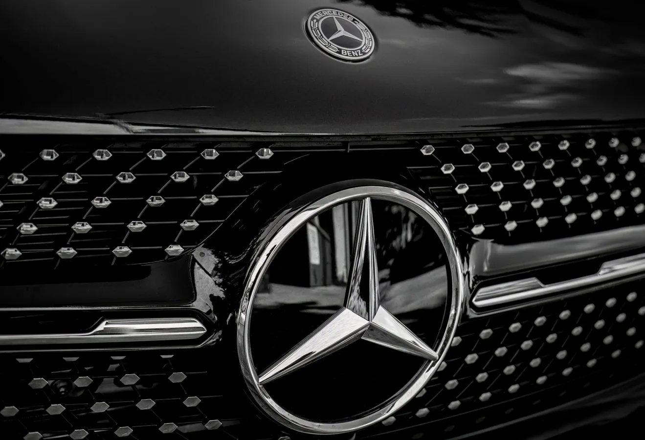 Detailed close-up of a Mercedes-Benz emblem on a luxury vehicle in black and white.