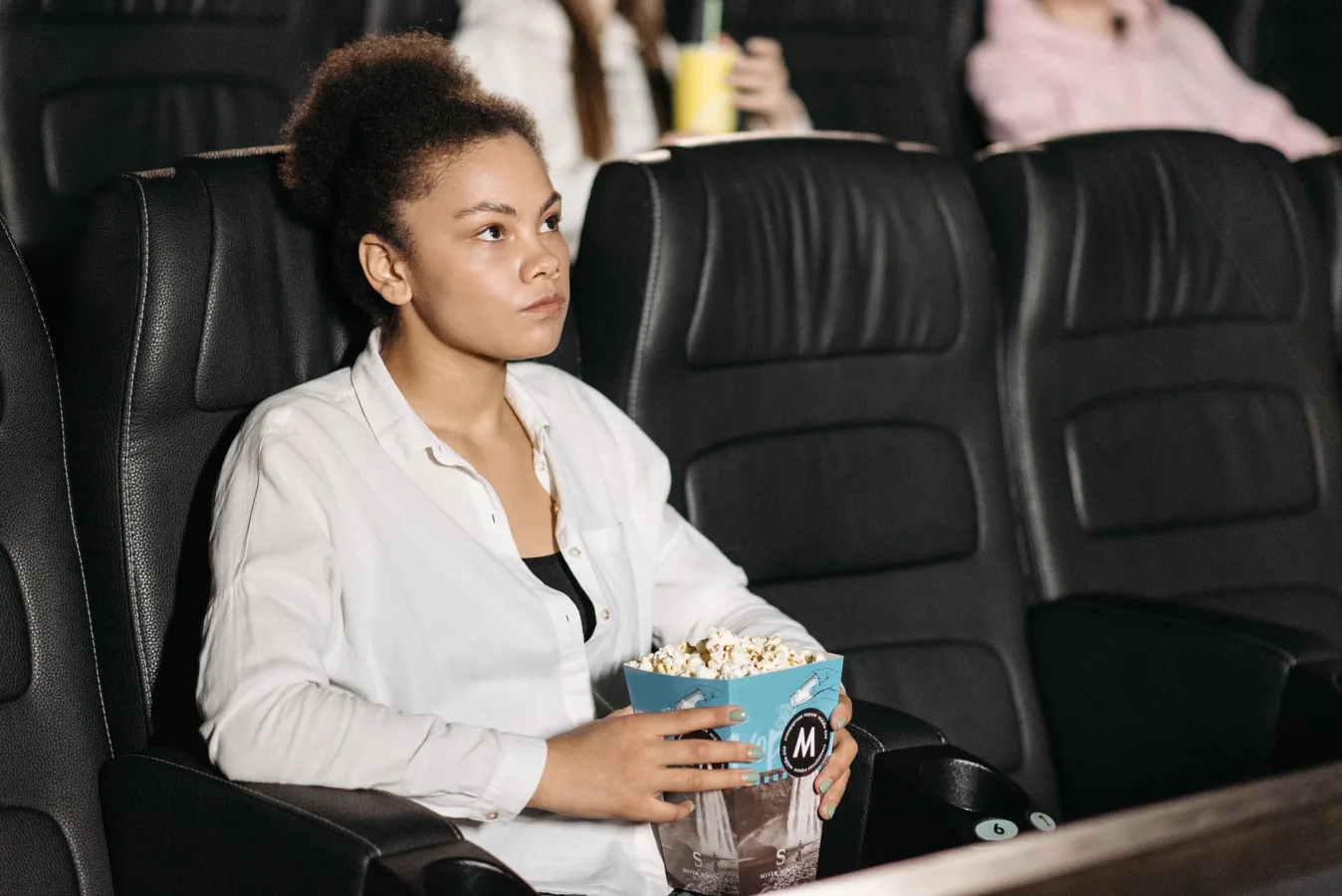 A woman sits in a movie theater holding popcorn, intently watching the screen.