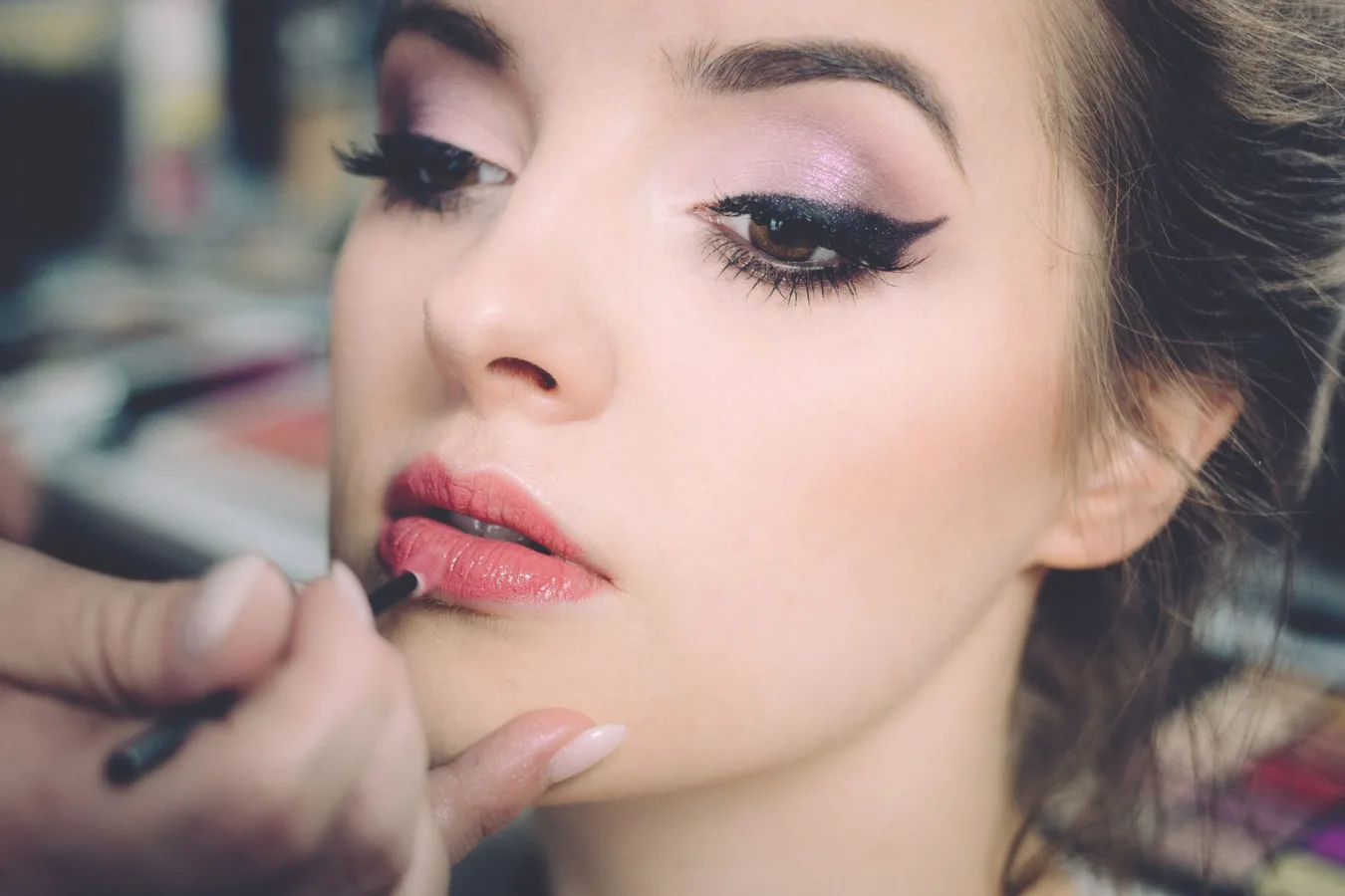 A close-up portrait of a woman getting professional makeup applied indoors, highlighting e