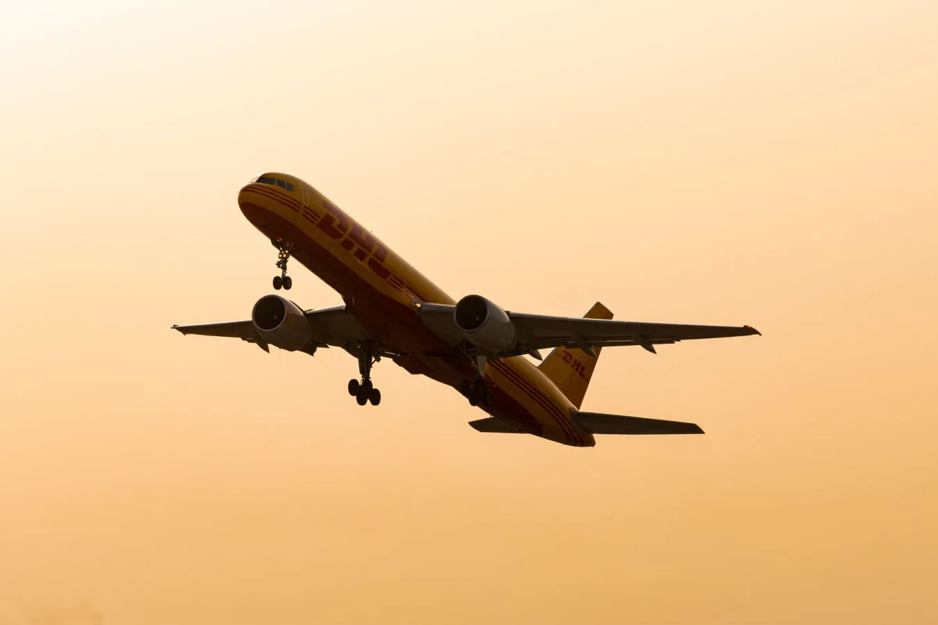 Cargo airplane flying in silhouette against a warm sunset sky.