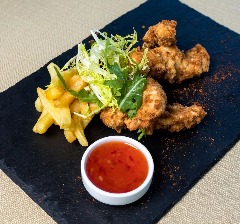 Mouthwatering plate of fried chicken with crispy fries and fresh salad on a black slate, s