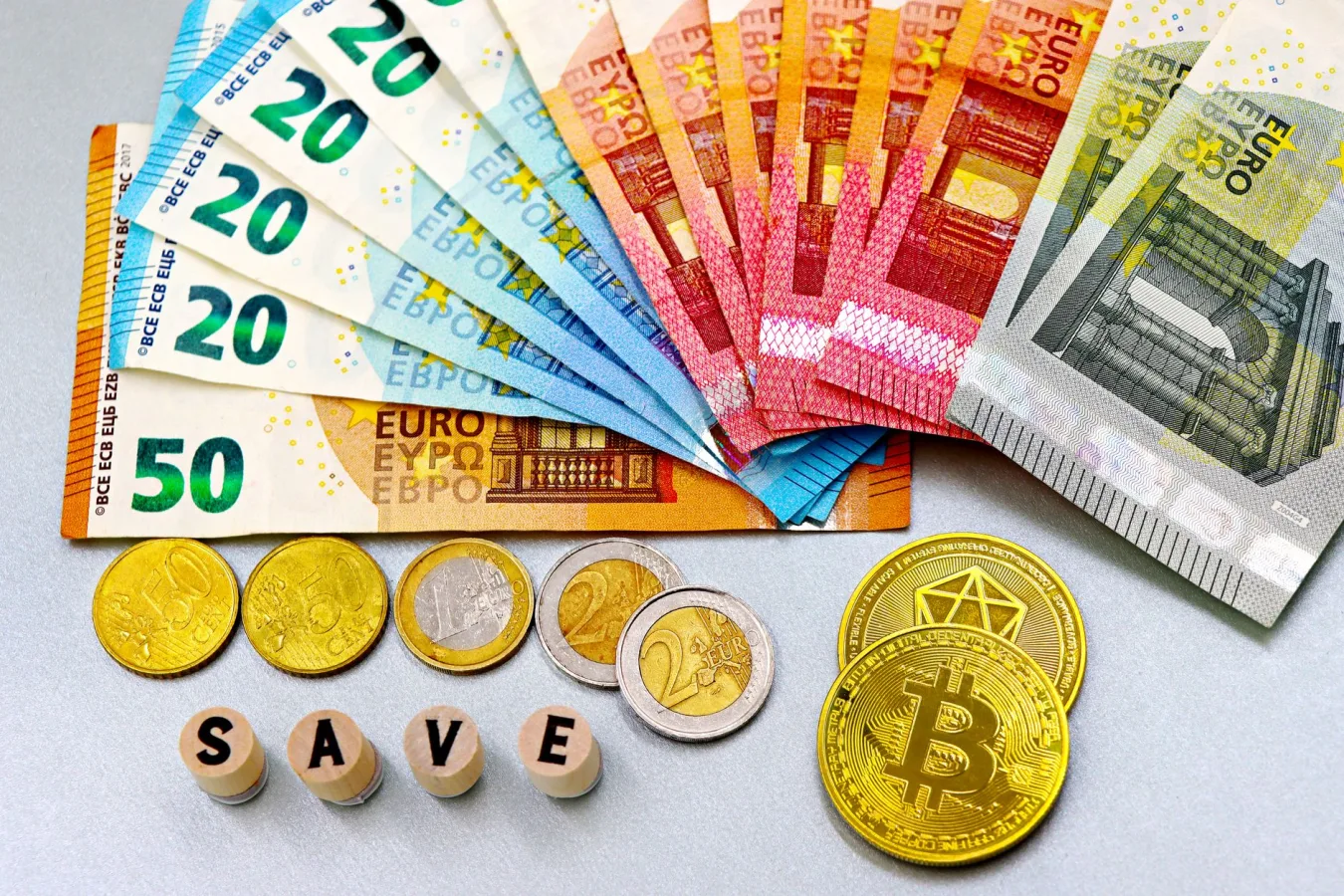 Euro banknotes and cryptocurrency coins arranged on a white surface with blocks spelling '