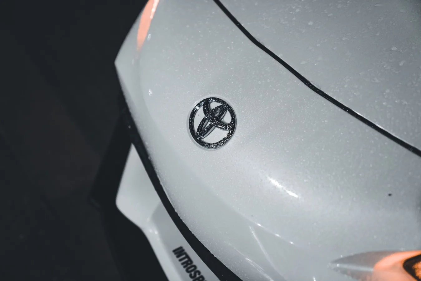 Detailed shot of a wet white car bonnet featuring the Toyota logo, highlighting texture an